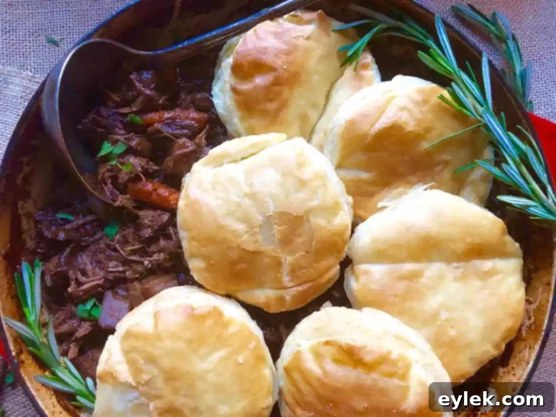 A hearty serving of braised beef stew with vegetables and a golden puff pastry