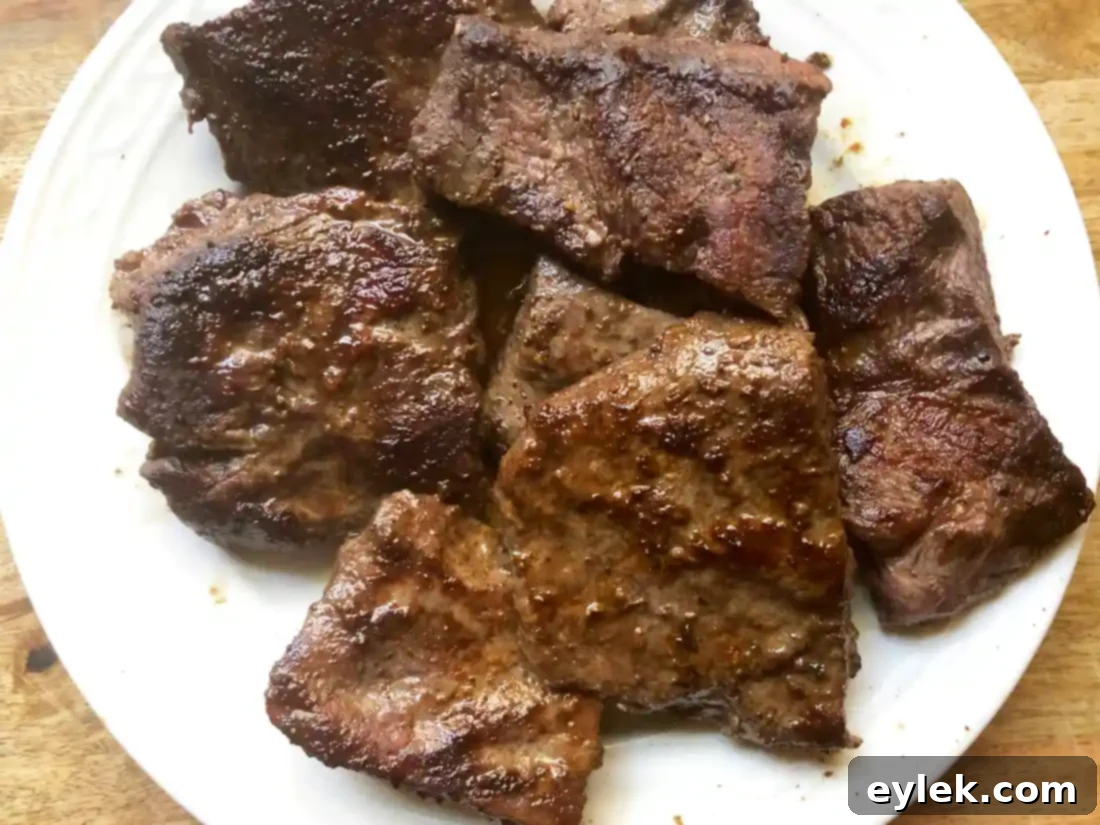 Seared beef resting on a plate with cooking drippings in the pot
