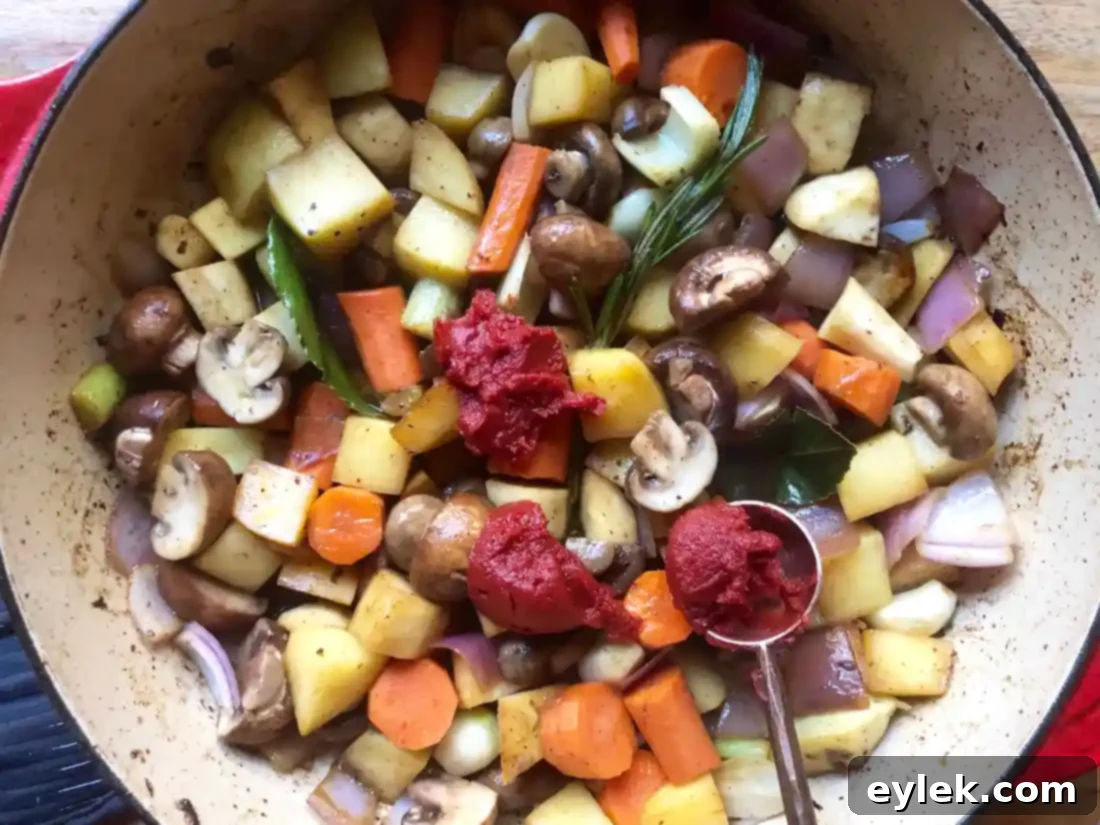 Tomato paste being mixed into sautéed vegetables and herbs