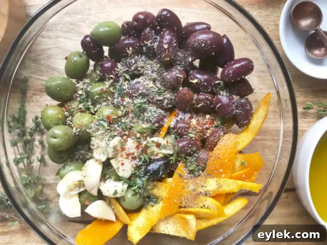 A mix of green and black olives tossed with orange zest, garlic, and fresh herbs in a bowl.