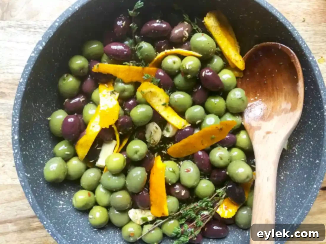 Close-up of freshly warmed marinated olives in a serving dish, garnished with fresh thyme.