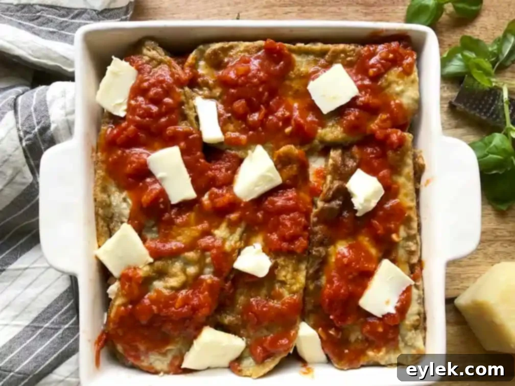Eggplant Parmesan layered with cheese, sauce, and basil, ready for final topping