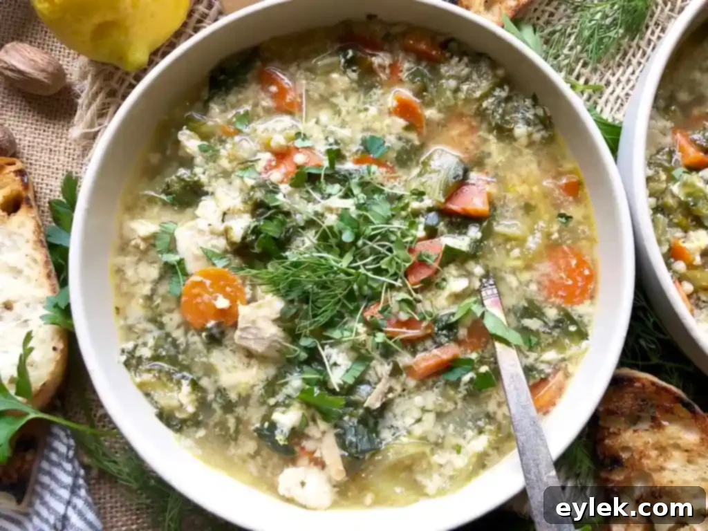 Close-up of a bowl of Chicken Escarole Soup with Egg & Pasta, garnished with fresh herbs and cheese.