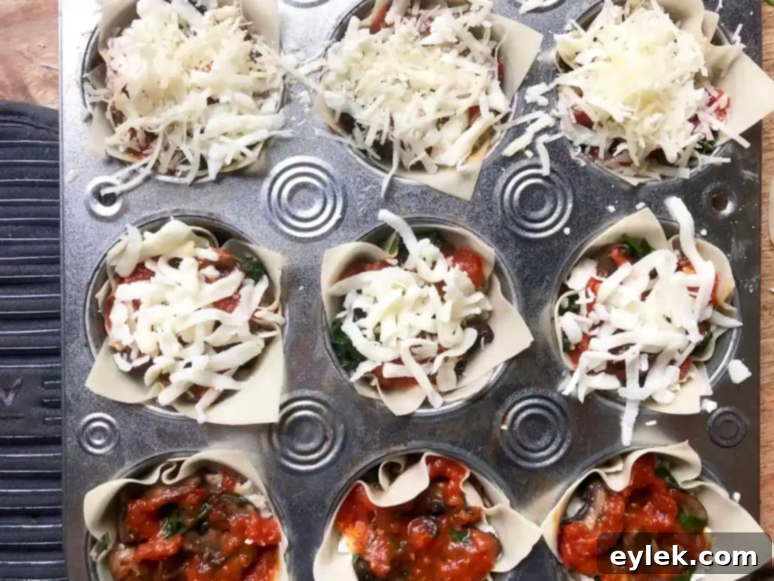 Close-up of the assembled veggie lasagna cups, topped with cheese and marinara, before baking.