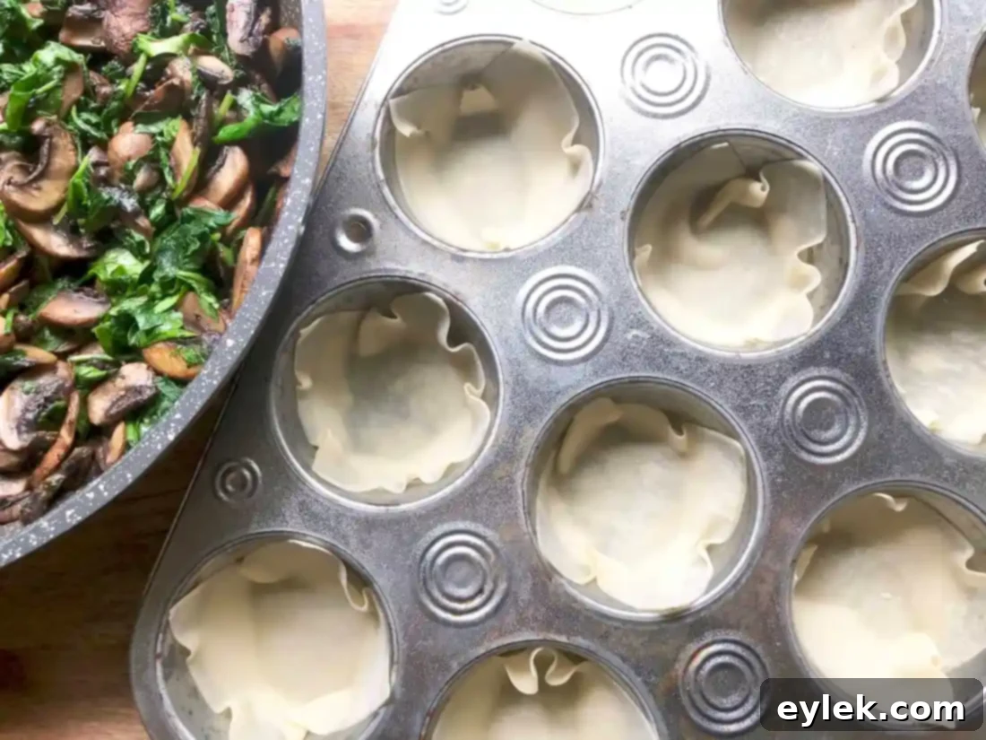 First layer of cheese, vegetables, and sauce in wonton cups for veggie lasagna.