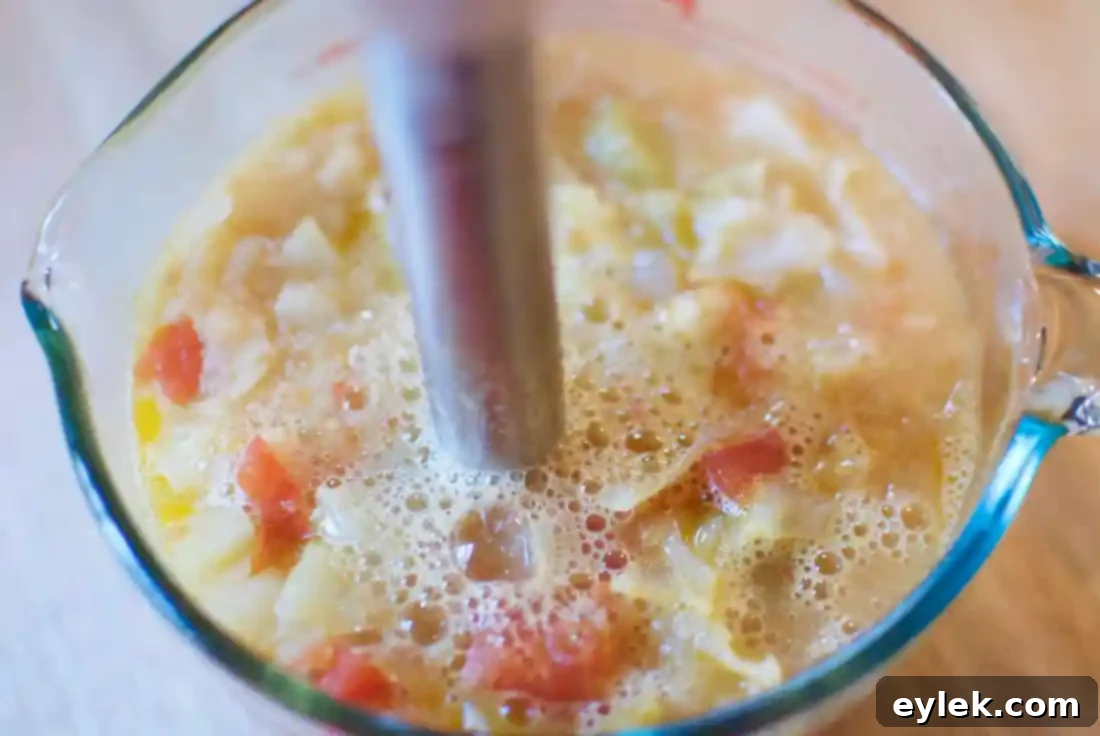The process of blending part of the minestrone with an immersion blender to achieve a creamy base.