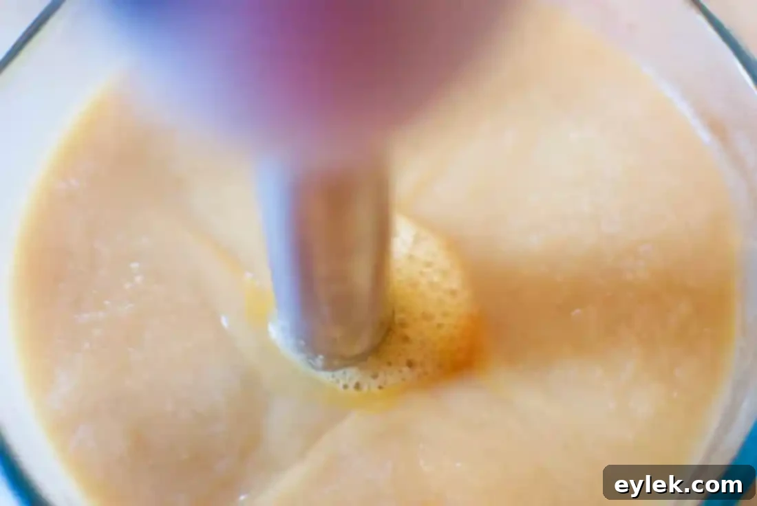 The blended minestrone portion being poured back into the main pot, adding creamy thickness to the soup.