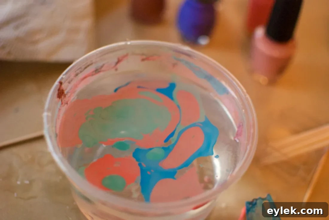 A hand gently dipping a hard-boiled egg into water with swirling nail polish for marble effect.