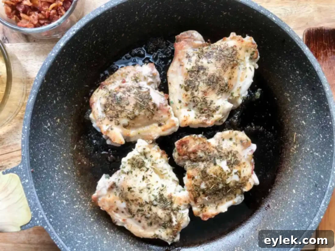 Seasoned chicken thighs browning in a skillet, creating a flavorful fond