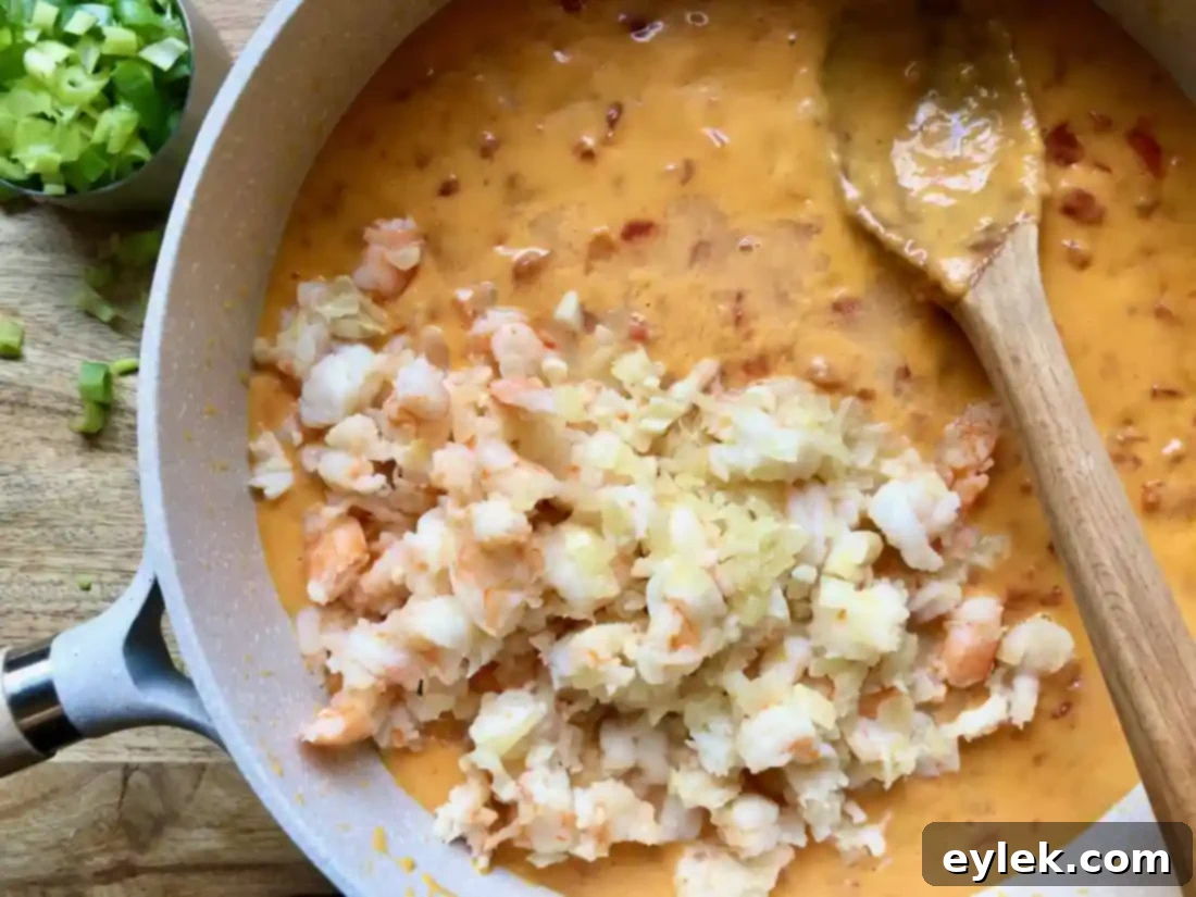 Mixing the shrimp and green onions into the melted queso for a vibrant finish.