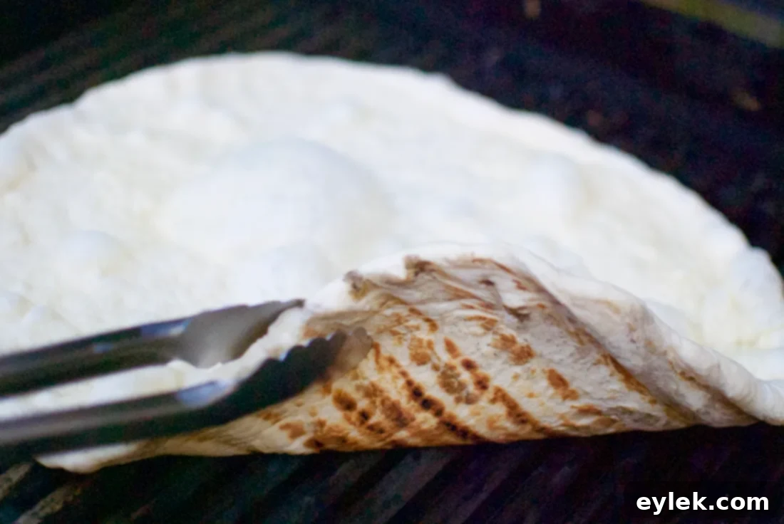 First side of pizza crust grilling on a barbecue, showing light char marks
