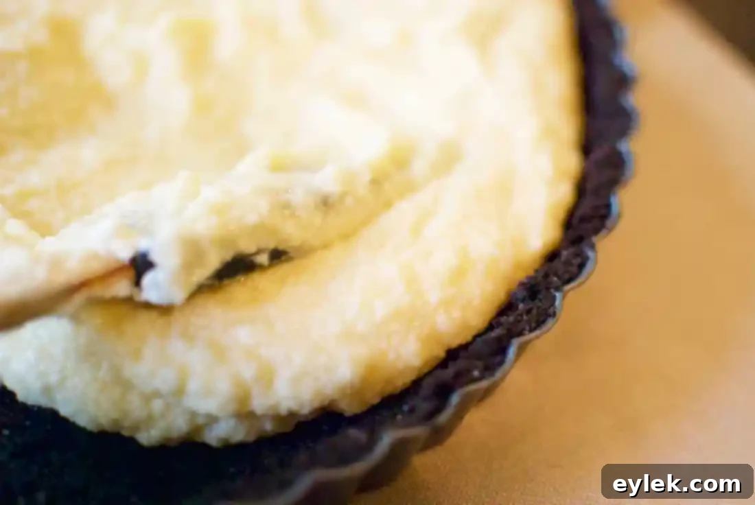 Mascarpone filling poured into the chocolate cookie crust in a tart pan, ready for baking.