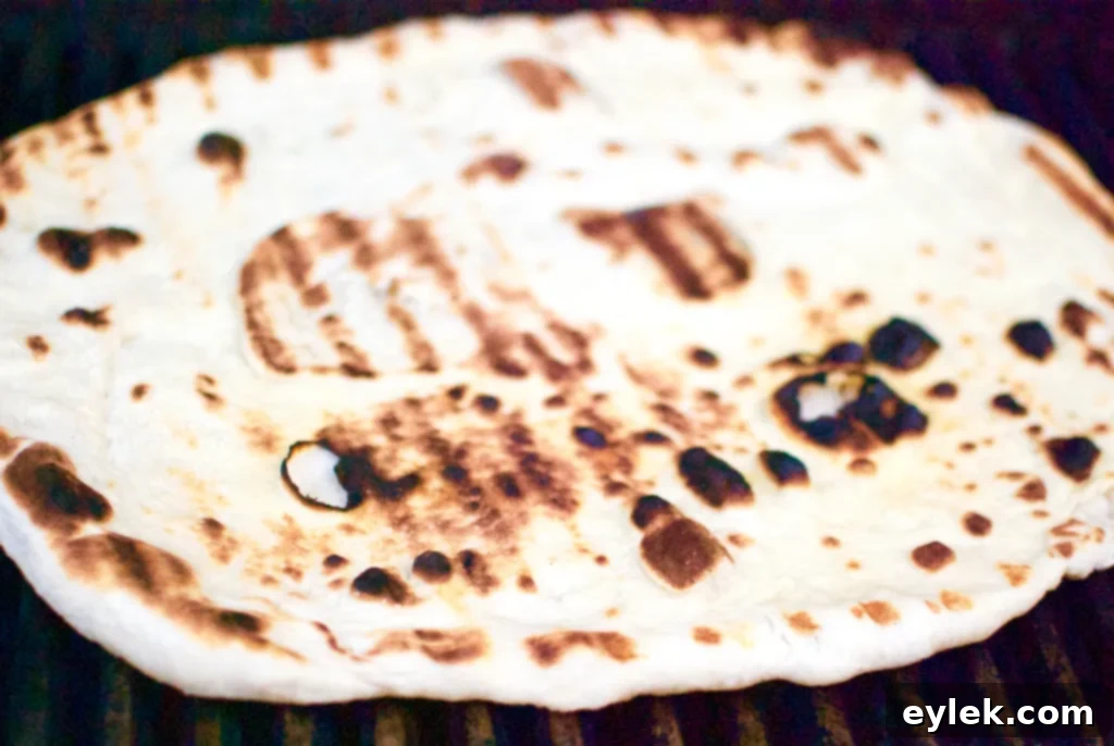 Grilled pizza crust being flipped on the grill