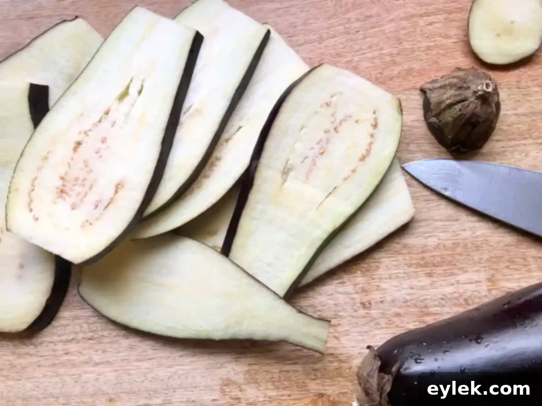 Thinly sliced eggplant laid out on paper towels, with a salt shaker nearby, ready for salting to draw out moisture and bitterness.