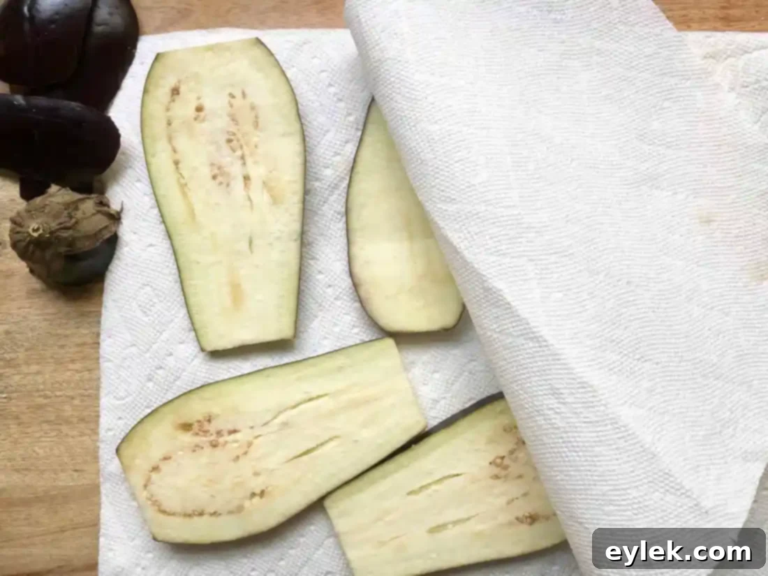 Close-up of salted eggplant slices releasing moisture onto paper towels, an essential step for preparing eggplant for sautéing.