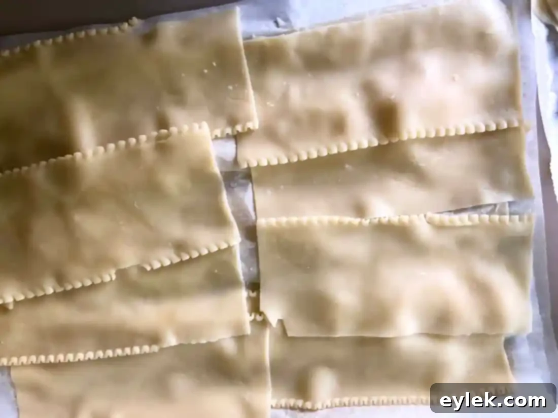 Cooked lasagna noodles laid out in a single layer on parchment paper to prevent sticking, with distinct wavy edges visible.