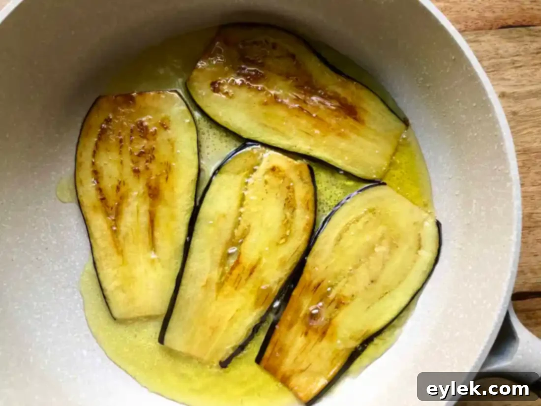 Sautéed eggplant slices achieving a rich golden brown color in a nonstick skillet, crucial for developing deep flavor and tender texture for the lasagna spirals.