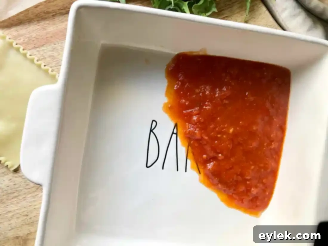 A square ceramic baking dish with a smooth, even layer of rich marinara sauce at the bottom, prepared to receive the eggplant lasagna spirals.