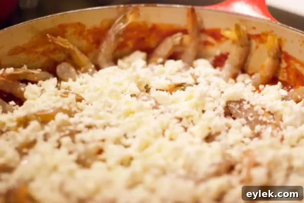 Crumbled feta cheese scattered over raw shrimp and tomato base