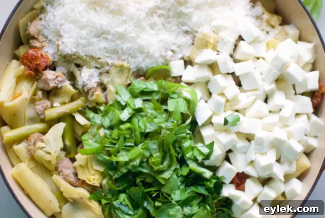 Plated Rigatoni with Sausage, Artichokes & Asparagus, garnished with fresh herbs and Parmesan cheese
