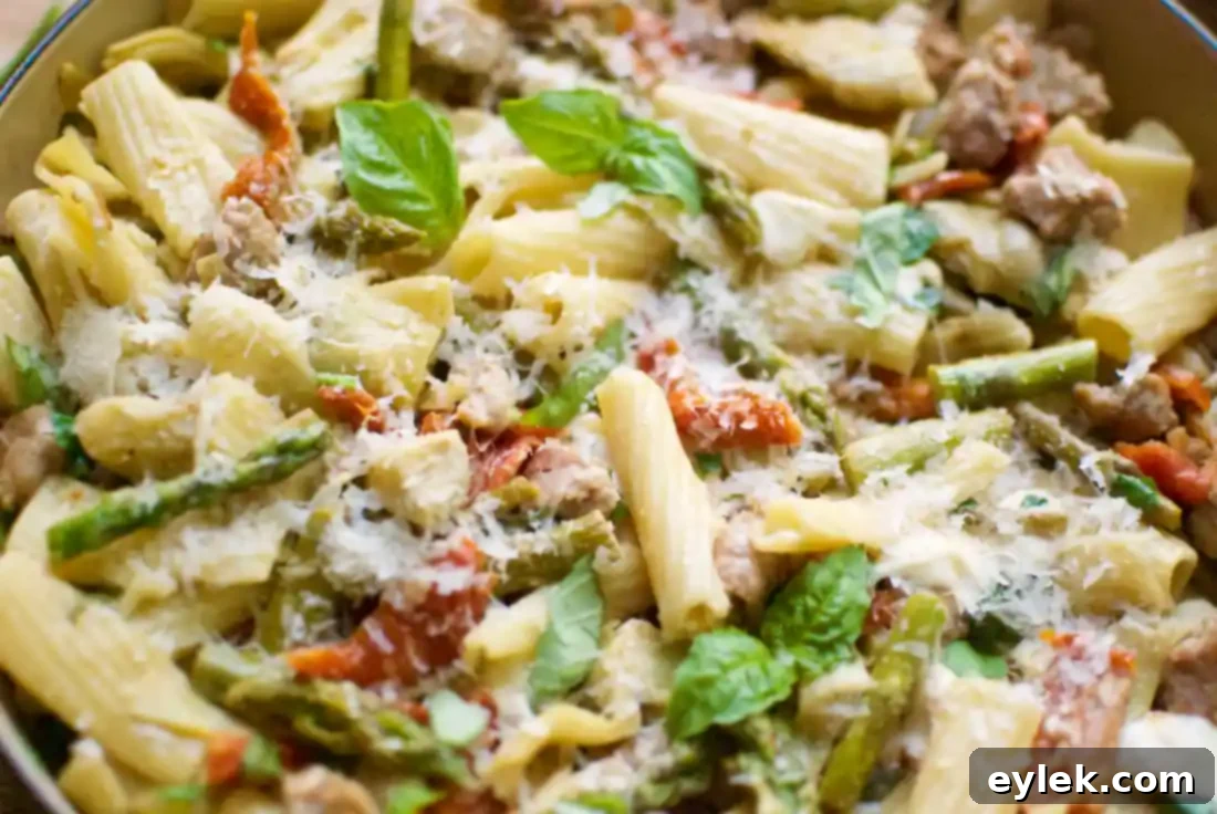 A large serving bowl filled with Rigatoni with Sausage, Artichokes & Asparagus, garnished and ready for a meal