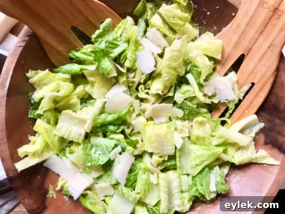Close-up of fresh romaine lettuce being perfectly coated in creamy Caesar dressing in a wooden bowl.