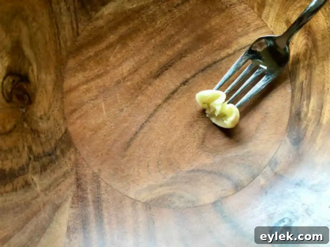 Detail shot of garlic clove being rubbed on the inside of a rustic wooden salad bowl, infusing it with flavor.