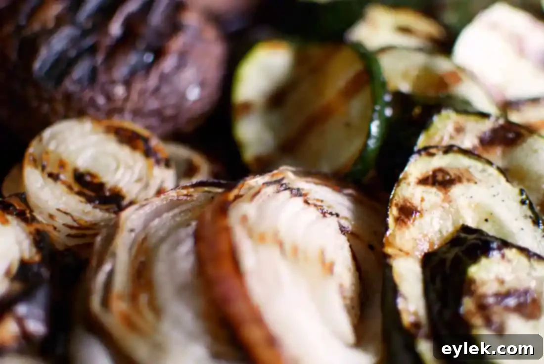 Grilled zucchini and onions on an outdoor grill, showing char marks.