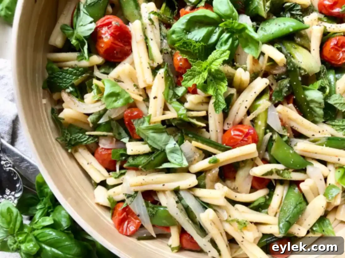 A bowl of pasta salad with spring vegetables and roasted tomatoes