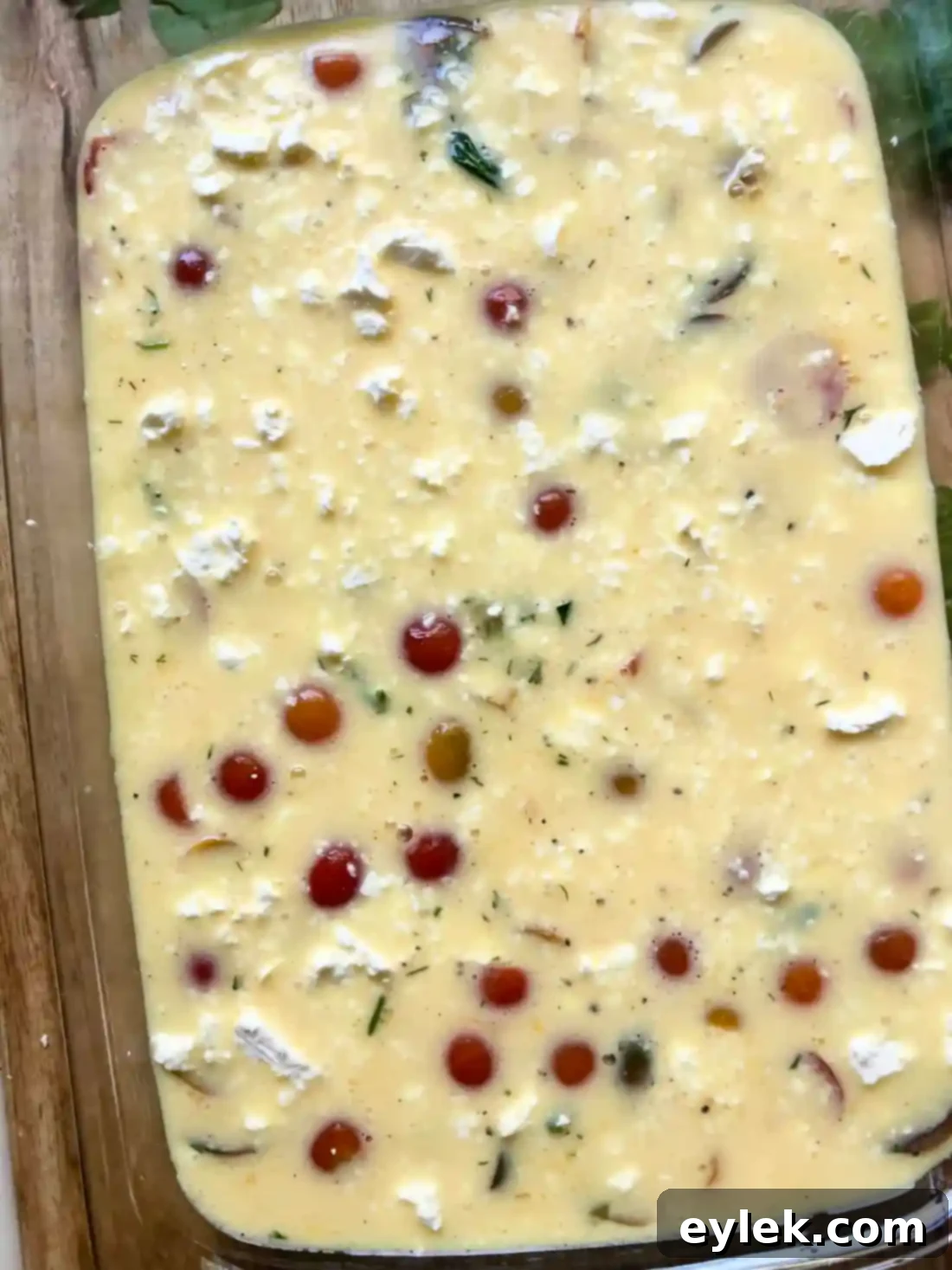 Pouring egg mixture over vegetables in baking dish