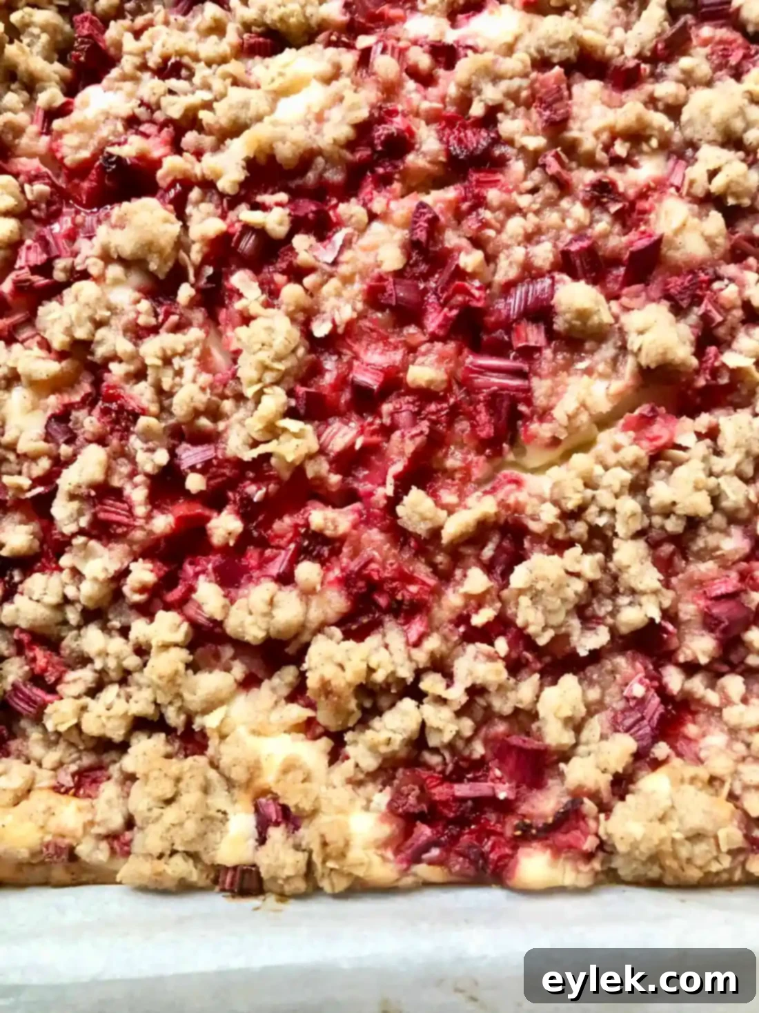 Freshly baked strawberry rhubarb cheesecake squares, glistening with fruit and golden crumble.