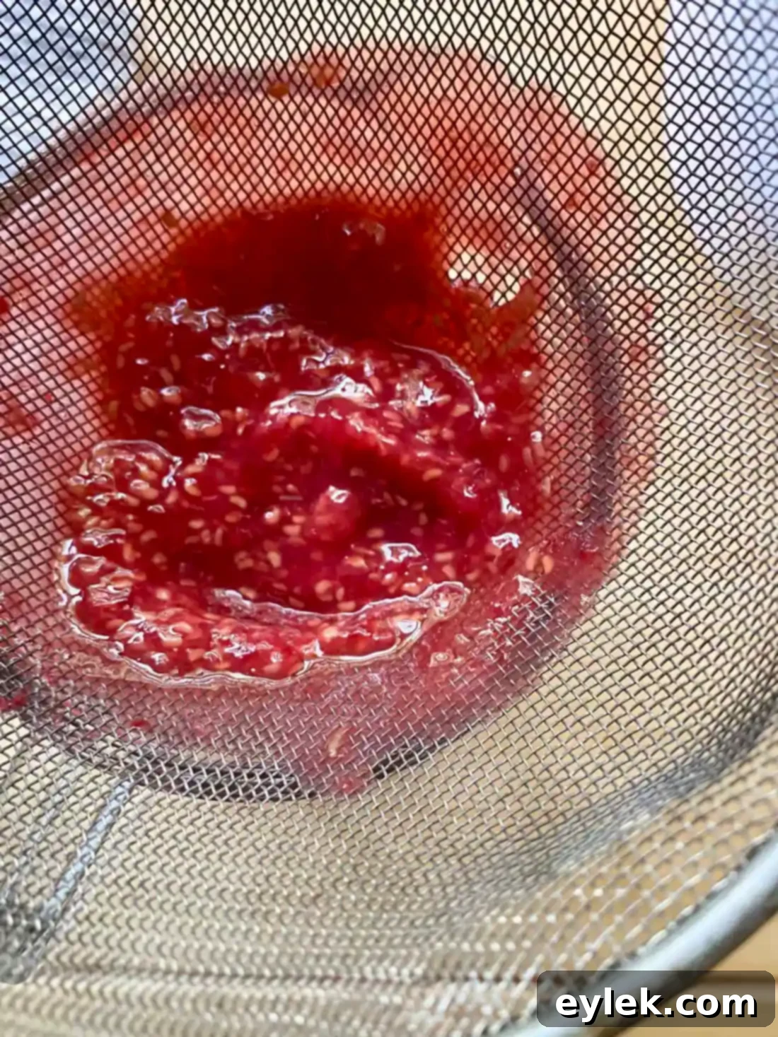 Raspberry seeds collected in a fine-mesh strainer