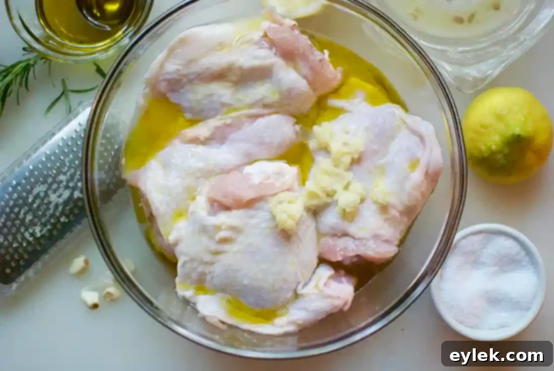 Chicken thighs marinating in a bowl with fresh lemon slices, minced garlic, and olive oil