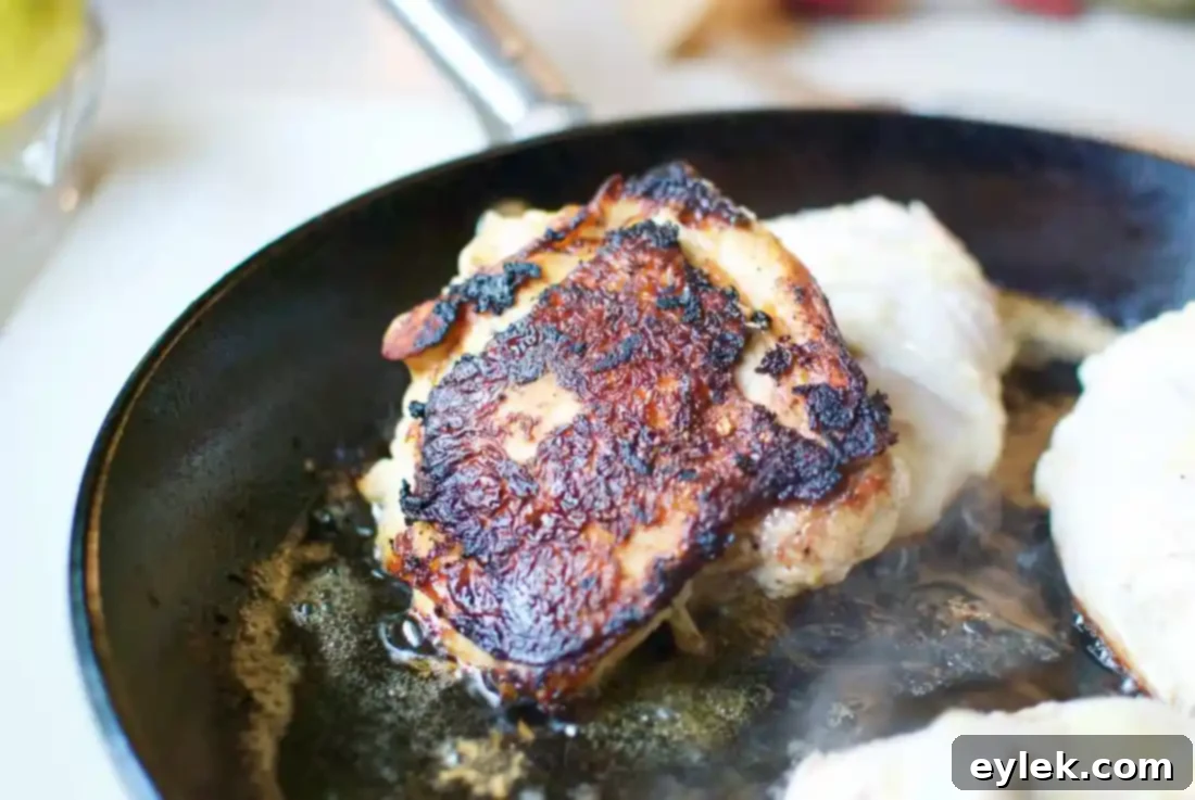Chicken thighs searing in a heavy cast iron skillet, achieving a deep brown char on the skin