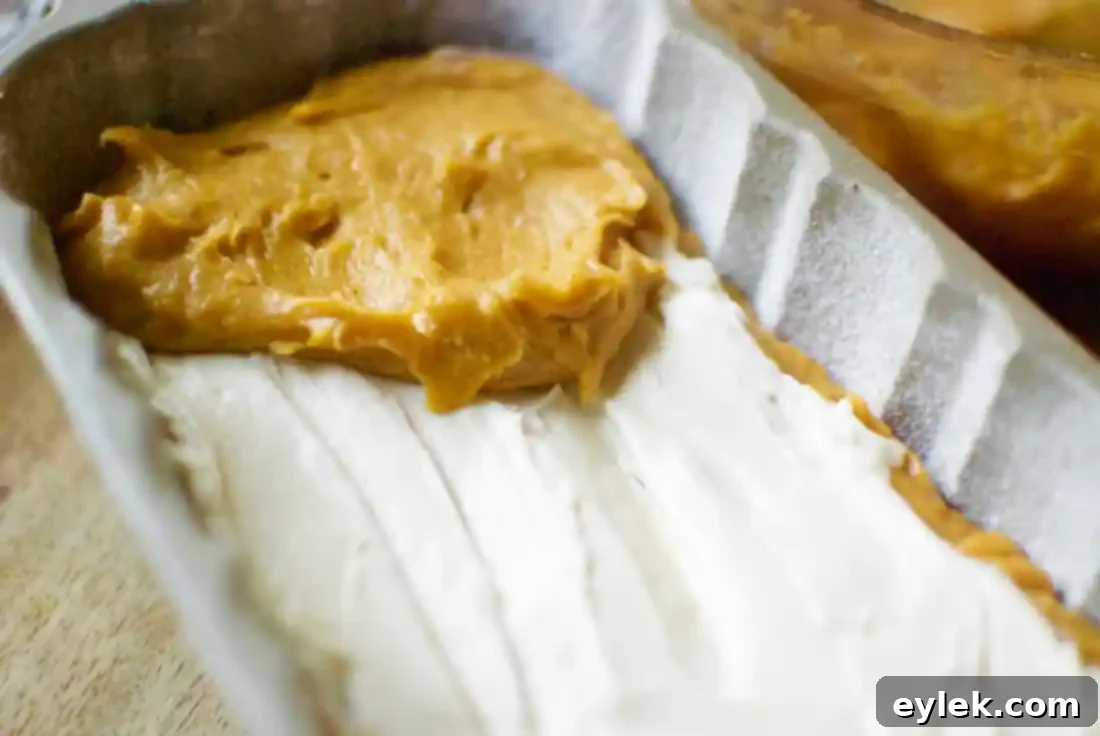 Half of pumpkin bread batter layered in the pan with cream cheese filling on top