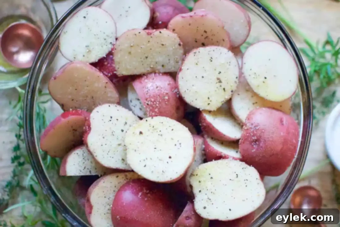 Halved potatoes mixed with olive oil, salt, and pepper in a bowl