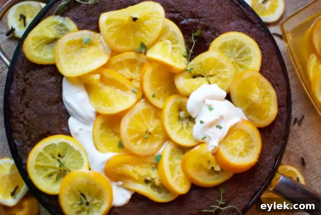 Close-up of a slice of Chocolate Gingerbread Cake with fresh whipped cream and simmered orange garnish