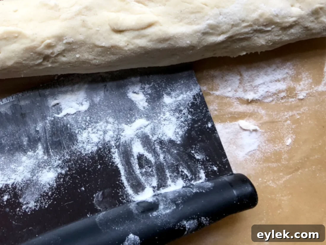 Gluten-Free Brioche dough being rolled into a log with a pastry scraper.