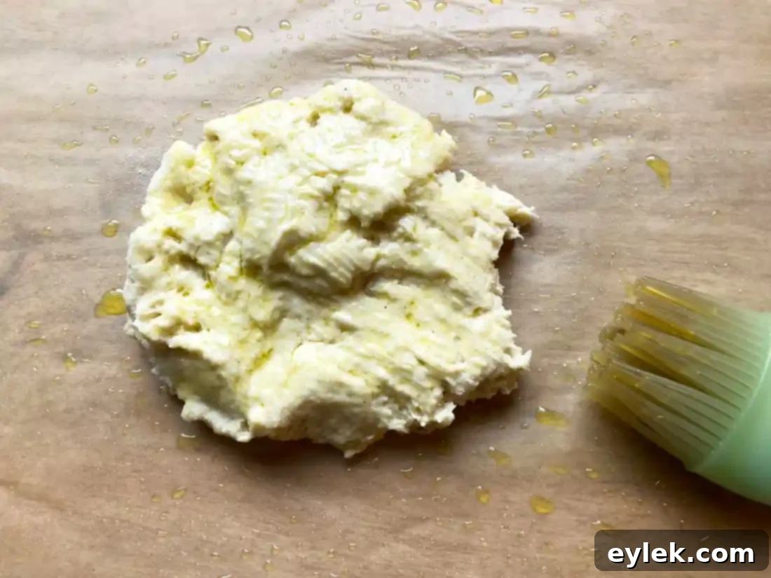 Gluten-free pizza dough being patted and drizzled with olive oil on parchment paper.