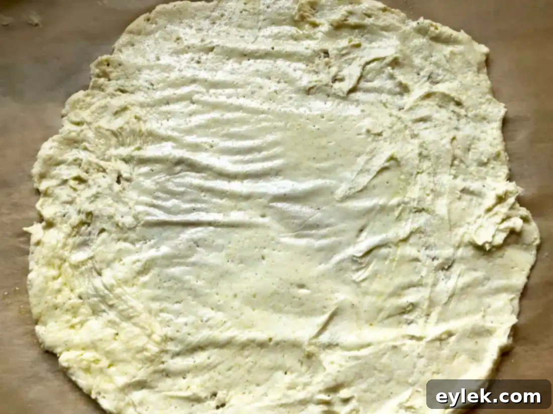 Gluten-free pizza dough covered with another sheet of parchment paper, ready for rolling.