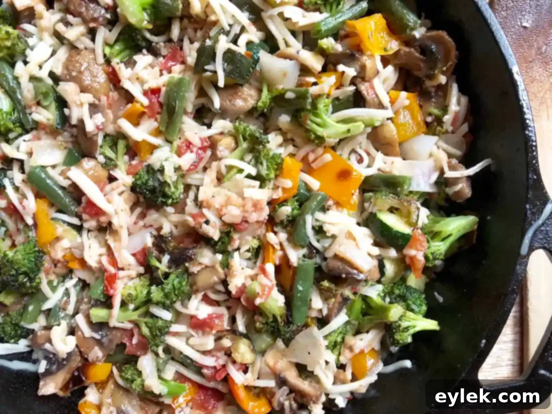 skillet filled with mixed roasted vegetables and shredded cheese, ready to bake