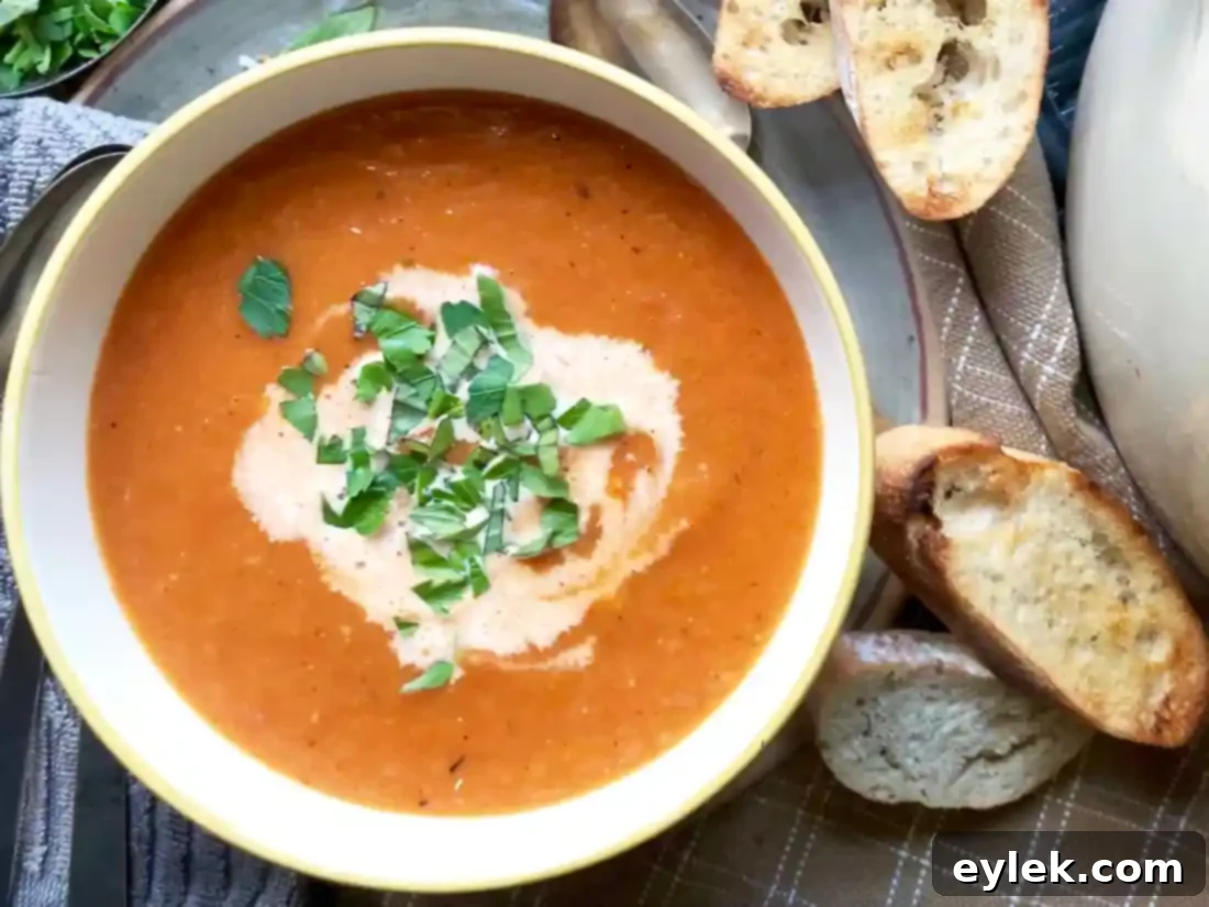 Two bowls of creamy roasted tomato soup, one with a dollop of cream, on a rustic wooden board.