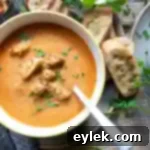 A bowl of creamy roasted tomato soup with a sprig of rosemary.