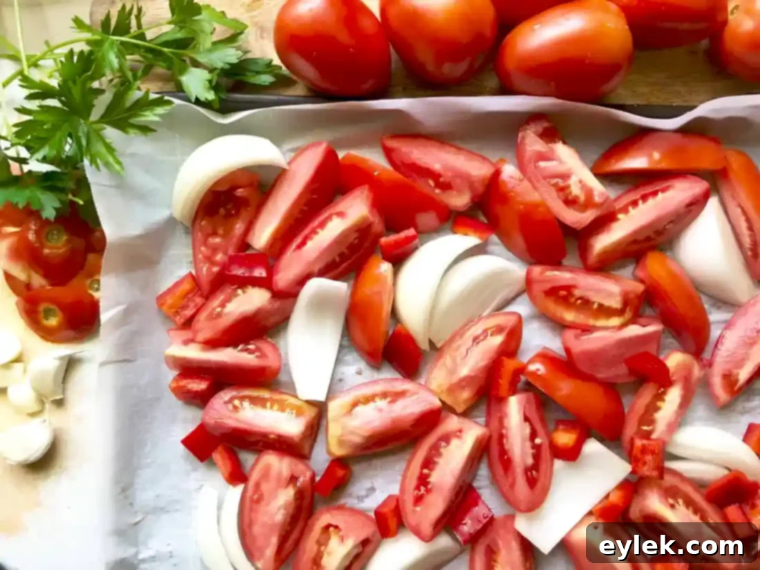 Tomatoes, onion, and red bell pepper arranged on parchment-lined baking sheets, drizzled with olive oil and seasoned with salt and pepper.