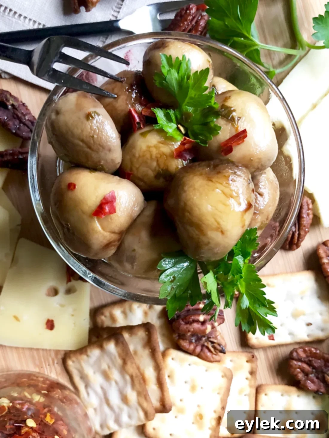 A tall, elegant serving of marinated mushrooms in a clear glass jar, garnished with herbs and lemon peel.
