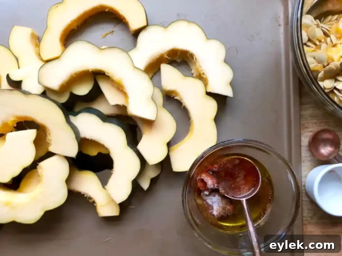 acorn squash slices tossed with spices and oil on baking sheet