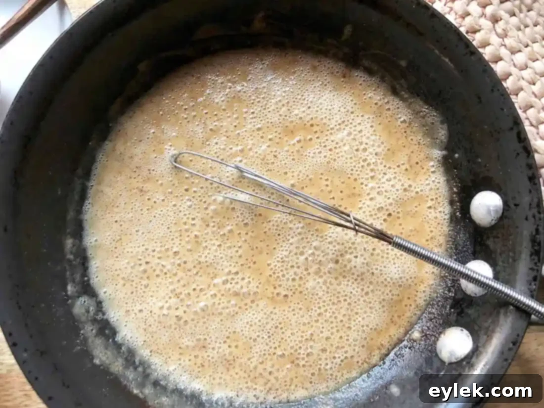 Adding broth to the roux, gradually whisking to prevent lumps.