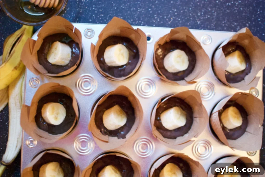 Muffin batter with banana slices and honey drizzle in a muffin tin