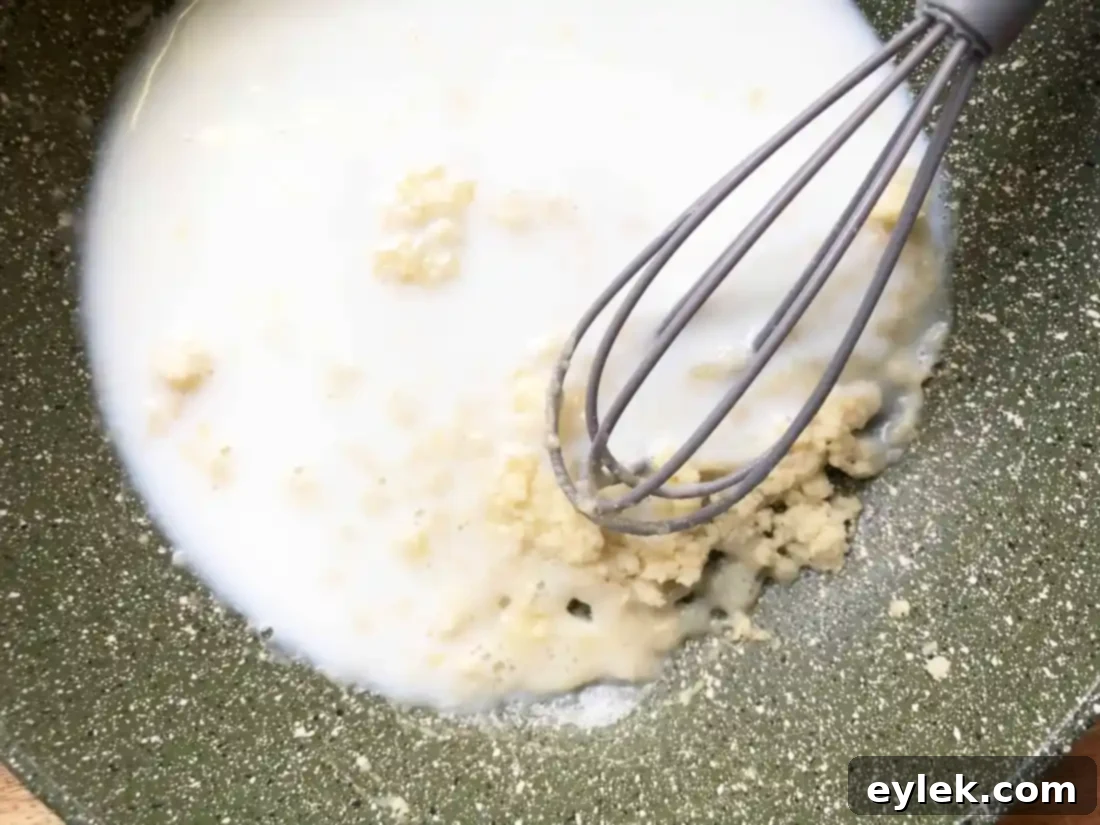 Milk being whisked into a roux in a saucepan.