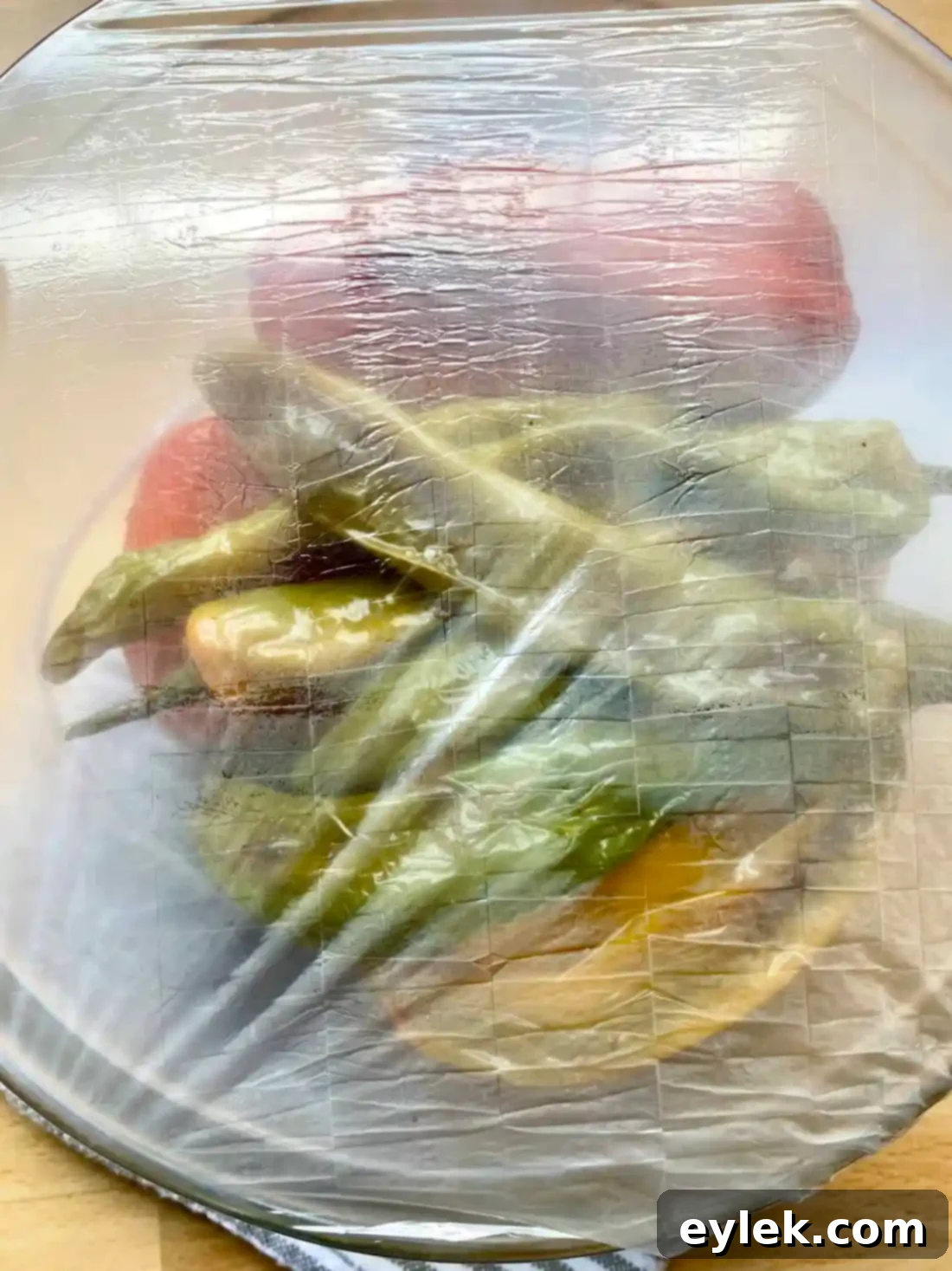 Bowl of peppers covered with plastic wrap to steam